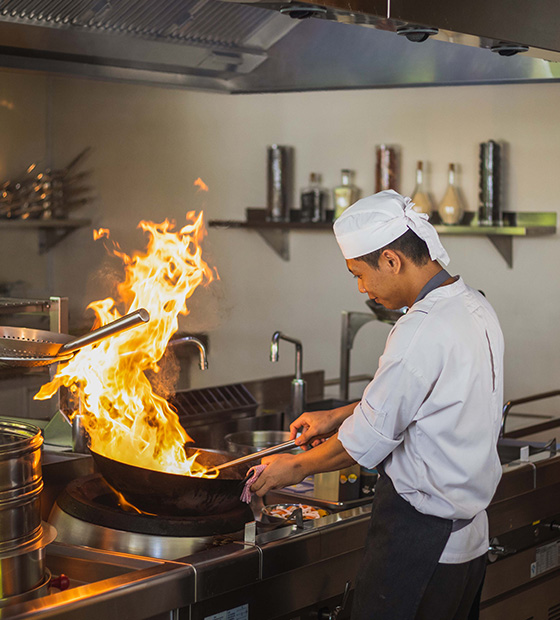 Chef skillfully handling a pan with flames while cooking at Kuda Villingili Maldives