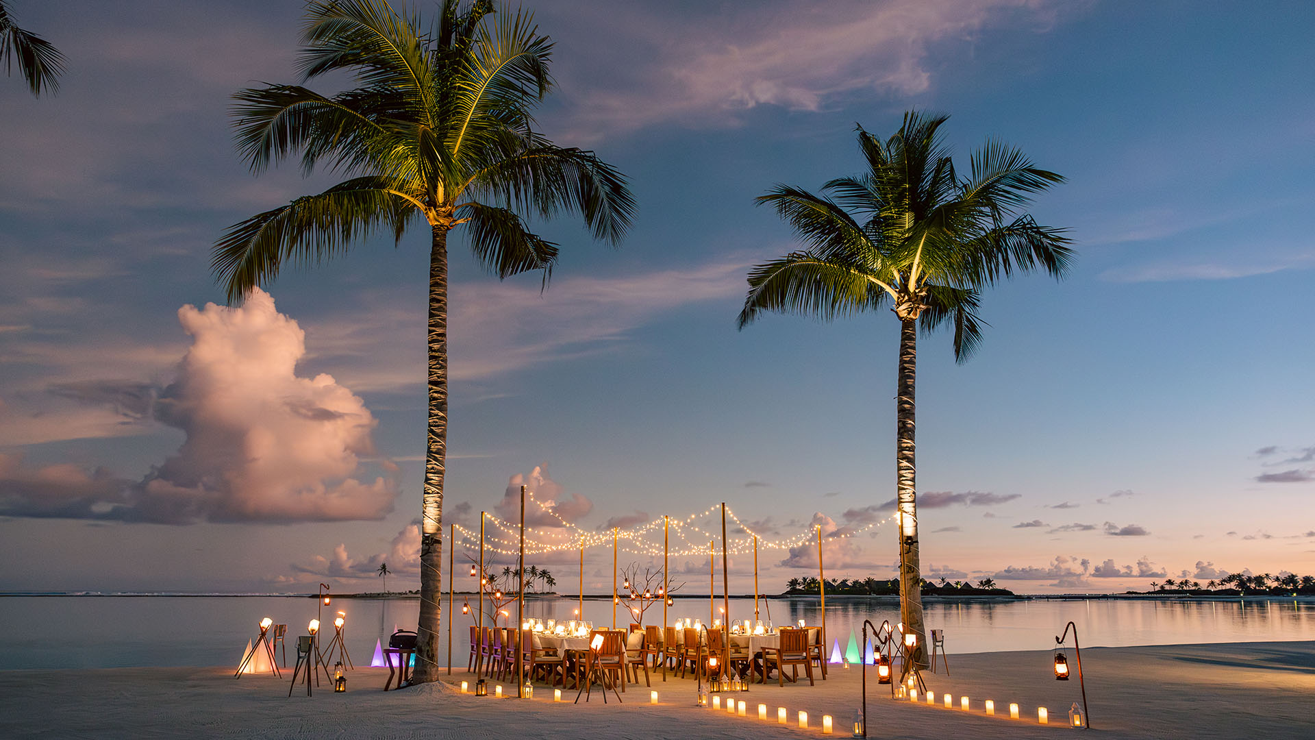 Beach dinner setup with two palm trees and soft lighting at Kuda Villingili Maldives