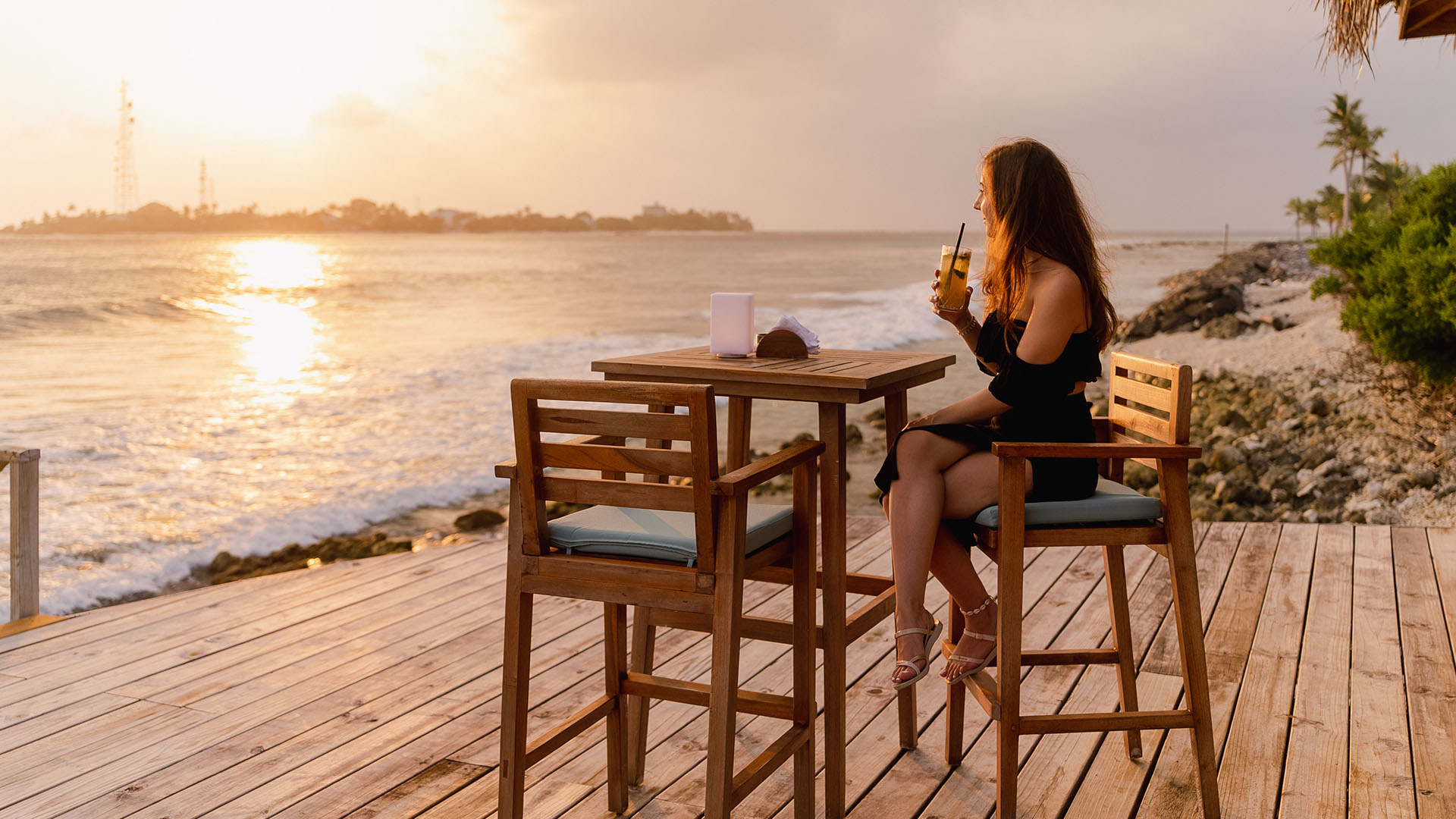 Guest holding a drink, enjoying sunset and sea view at Kuda Villingili Maldives