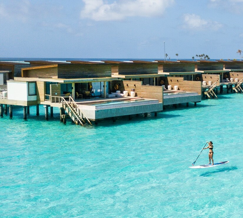 Overwater villas at Kuda Villingili Maldives with a guest paddleboarding